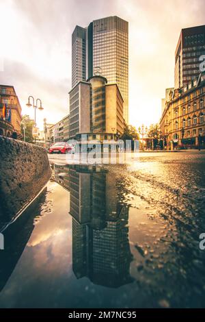 Blick auf eine Schlucht am Morgen. Mit Sonnenlicht und Reflexion in einer Pfütze auf der Straße in Frankfurt am Main, Hessen Stockfoto