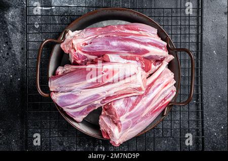 Rohe Lammschenkelschäfte in einer Stahlschale mit Kräutern. Schwarzer Hintergrund. Draufsicht. Stockfoto