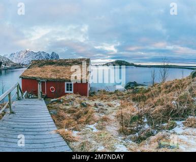 Traditionelle Rorbu Hütte / Haus in Lofoten, Norwegen, typische Fjordlandschaft mit Bergen, Fischerdorf und Meerblick Stockfoto