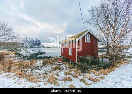 Traditionelle Rorbu Hütte / Haus in Lofoten, Norwegen, typische Fjordlandschaft mit Bergen, Fischerdorf und Meerblick Stockfoto