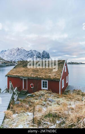 Traditionelle Rorbu Hütte / Haus in Lofoten, Norwegen, typische Fjordlandschaft mit Bergen, Fischerdorf und Meerblick Stockfoto