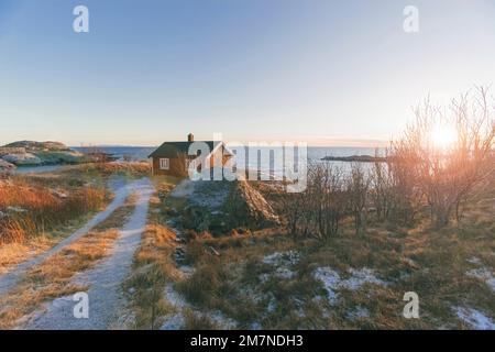 Traditionelle Rorbu Hütte / Haus in Lofoten, mit Zufahrtsstraße bei Sonnenuntergang, Norwegen, typische Fjordlandschaft, Fischerdorf und Meerblick Stockfoto