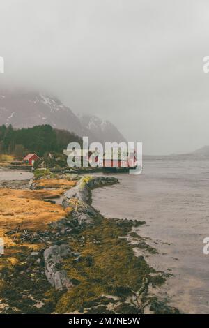 Drei rote einsame Fischerhütten auf dem Fjord in Norwegen, typische Fjordlandschaft mit kleinen Inseln, Abgeschiedenheit von der Außenwelt, Bootshaus Stockfoto