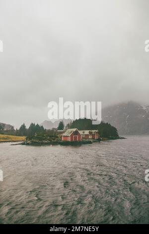 Drei rote einsame Fischerhütten auf dem Fjord in Norwegen, typische Fjordlandschaft mit kleinen Inseln, Abgeschiedenheit von der Außenwelt, Bootshaus Stockfoto