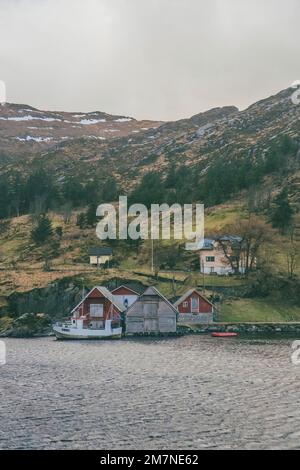 Zwei kleine Fischerhäuser auf dem Fjord ö€°heö ˆlesund in Norwegen, typische Fjordlandschaft mit kleinen Inseln, Abgeschiedenheit von der Außenwelt, rotes Bootshaus am Meer. Stockfoto