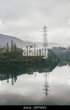 Einsames Haus auf der Insel mit großem Kraftmast in Norwegen, Landschaft mit Reflexion im Wasser, typische Fjordlandschaft mit kleinen Inseln, Isolation von der Außenwelt Stockfoto