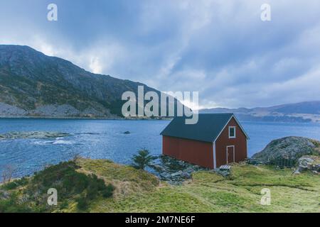 Einsame rote Fischerhütte am Fjord in Norwegen, typische Fjordlandschaft mit kleinen Inseln, Abgeschiedenheit von der Außenwelt, Haus am Meer, ikonische Hütte Stockfoto