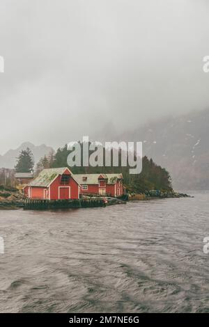 Drei rote einsame Fischerhütten auf dem Fjord in Norwegen, typische Fjordlandschaft mit kleinen Inseln, Abgeschiedenheit von der Außenwelt, Bootshaus Stockfoto