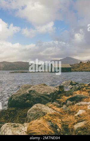 Einsames Steinhaus am Fjord in Norwegen, typische Fjordlandschaft mit kleinen Inseln, Abgeschiedenheit von der Außenwelt, Haus am See, Bootshaus Stockfoto