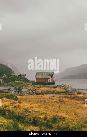 Eine rote einsame Fischerhütte am Fjord in Norwegen, typische Fjordlandschaft mit kleinen Inseln, Abgeschiedenheit von der Außenwelt, Bootshaus, zentriert Stockfoto