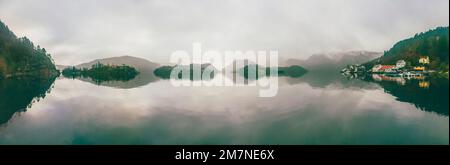 Panoramabild des Fjords mit Inselgruppe, Fischerhütten, Häusern, Booten, Strommasten in Norwegen, Landschaft mit einsamem Fischerdorf, typische Fjordlandschaft mit kleinen Inseln, Skandinavien Stockfoto