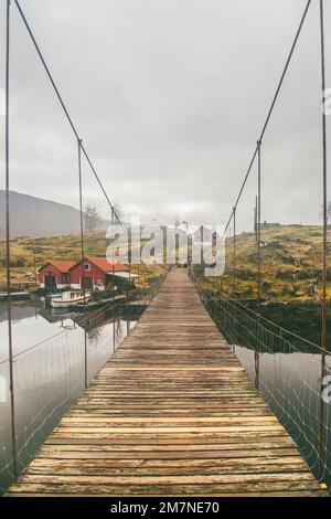 Alte hölzerne Hängebrücke im Fjord, Inselgruppen mit Fischerhütten, Häuser, Boote, Strommasten in Norwegen, Landschaft mit einsamem Fischerdorf, typische Fjordlandschaft mit kleinen Inseln, Skandinavien Stockfoto