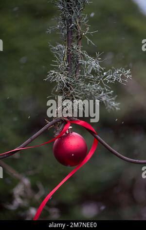 Eine rote Weihnachtsbaumkugel hängt draußen während des Schneefalls Stockfoto