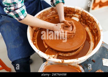 Zugeschnittenes Bild eines nicht wiedererkennbaren weiblichen Keramikmachers, das mit dem Keramikrad in Cozy Workshop arbeitet, macht eine Vase oder Tasse der Zukunft, kreatives Handwerk für Menschen Stockfoto