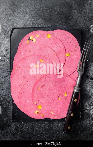 Scheiben von Fleischsalami-Wurst mit Pistaziennüssen auf Marmorbrett. Schwarzer Hintergrund. Draufsicht. Stockfoto