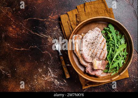 Gebratene Schweinekoteletts oder Koteletts mit Rucola-Salat. Dunkler Hintergrund. Draufsicht. Speicherplatz kopieren Stockfoto