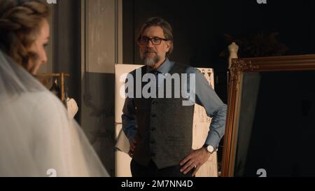 Filmaufnahme einer Frau im Hochzeitskleid, die in den Spiegel schaut und mit einem männlichen, reifen Schneider spricht. Braut im Designer-Atelier oder im Hochzeitssalon ein passendes Hochzeitskleid. Modebegriff und Couturier. Stockfoto