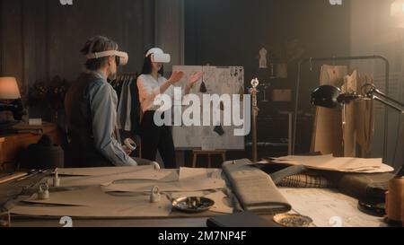 Schneiderinnen tragen VR-Headset mit schnurlosen Controllern. Sie arbeiten in einem Luxusatelier oder einer Schneiderwerkstatt und erstellen Unkrautanzüge in virtueller Realität. Konzept der Zukunftstechnologien in der Wirtschaft. Stockfoto