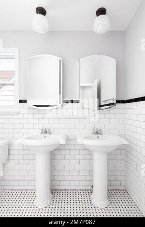 Ein Badezimmer mit zwei Standwaschbecken, gefliestem Boden und Wand und Lampen darüber. Stockfoto