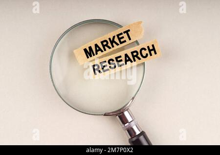 Auf der Lupe befinden sich Papierstreifen mit der Aufschrift „Market Research“. Stockfoto