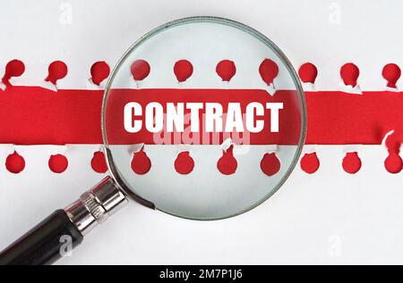 Zwischen zwei Blättern aus einem Notizbuch auf einem roten Streifen mit der Aufschrift „Contract“ befindet sich eine Lupe. Stockfoto