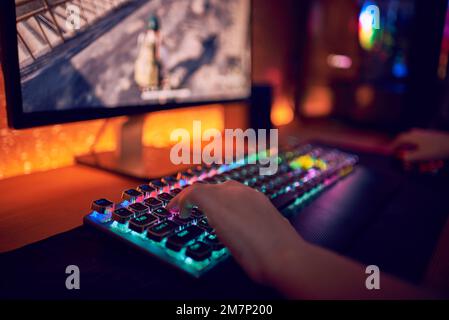 Nahaufnahme Handaufnahme eines Spielers beim Drücken der Tasten auf der Tastatur während eines Online-Videospiels. Tastatur-Led-Leuchten. Der Raum ist dunkel. Stockfoto