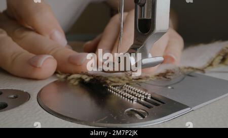 Die Hände der weiblichen Näherin arbeiten an der Nähmaschine. Designer näht Stoff in Atelier Nähwerkstatt. Konzept von Kleinunternehmen, Schneiderei, Handwerk und Mode. Extreme Nahaufnahme. Stockfoto