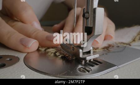 Die Hände der weiblichen Näherin arbeiten an der Nähmaschine. Designer näht Stoff in Atelier Nähwerkstatt. Konzept von Kleinunternehmen, Schneiderei, Handwerk und Mode. Makro Stockfoto