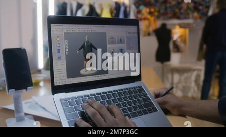 Afroamerikanischer Modedesigner kreiert Kleidung in 3D-Modelliersoftware auf einem Laptop mit digitalem Tablet und Eingabestift. Er arbeitet in der Atelier-Werkstatt. Mode- und Technologiekonzept in der Wirtschaft. Stockfoto