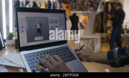 Afroamerikanischer Modedesigner kreiert Kleidung in 3D-Modelliersoftware auf einem Laptop mit digitalem Tablet und Eingabestift. Er arbeitet in der Atelier-Werkstatt. Mode- und Technologiekonzept in der Wirtschaft. Stockfoto