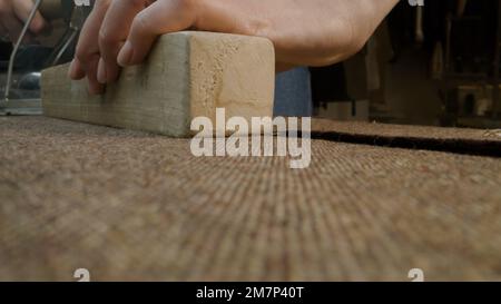 Die Hände von weiblichen Schneidebügeln mit Holzwerkzeugen. Atelier-Nähwerkstatt im Hintergrund. Konzept für Kleinunternehmen, Schneidereiindustrie, Mode und Handwerk. Nahaufnahme. Stockfoto