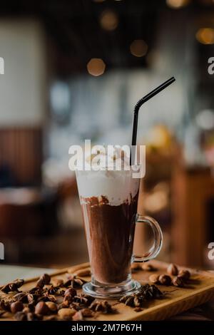 Eine heiße Schokolade aus nächster Nähe in einem großen Glas mit Schlagsahne auf einem Holzbrett in einem Café Stockfoto