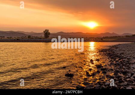 Sonnenuntergang Chatfield 2020 - die untergehende Sonne scheint durch den dichten Dunst des Rauchs mehrerer Waldbrände in den Rocky Mountains auf das ruhige Wasser des Chatfield Lake. Stockfoto