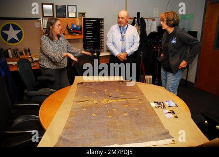 Susan Anderson (rechts) bietet einige Einblicke in die Flagge des Bundesstaates Indiana, die sie als Artefakt an das Hampton Roads Naval Museum spendet, an den Museumserzieher Zach Smyers (Mitte) und die stellvertretende Direktorin Toni Deetz-Rock (links). Die Flagge gehörte Andersons Vater, dem verstorbenen Captain Walter "Jack" Deal, USN, der während des Vietnamkriegs der befehlshabende Offizier des River Assault Squadron 15 war. Damals war es üblich, dass Bootskapitäne während des Vietnamkriegs die Staatsflagge ihres Heimatstaates auf ihren Flussangriffsbooten führten. Stockfoto