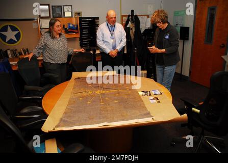 Susan Anderson (rechts) bietet einige Einblicke in die Flagge des Bundesstaates Indiana, die sie als Artefakt an das Hampton Roads Naval Museum spendet, an den Museumserzieher Zach Smyers (Mitte) und die stellvertretende Direktorin Toni Deetz-Rock (links). Die Flagge gehörte Andersons Vater, dem verstorbenen Captain Walter "Jack" Deal, USN, der während des Vietnamkriegs der befehlshabende Offizier des River Assault Squadron 15 war. Damals war es üblich, dass Bootskapitäne während des Vietnamkriegs die Staatsflagge ihres Heimatstaates auf ihren Flussangriffsbooten führten. Stockfoto