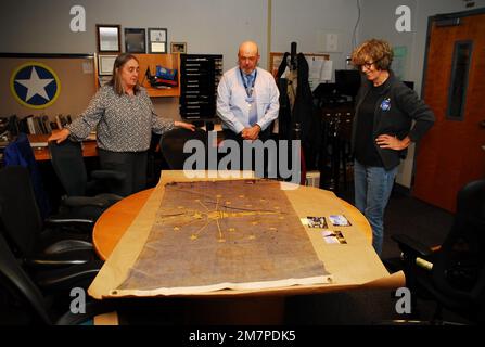 Susan Anderson (rechts) bietet einige Einblicke in die Flagge des Bundesstaates Indiana, die sie als Artefakt an das Hampton Roads Naval Museum spendet, an den Museumserzieher Zach Smyers (Mitte) und die stellvertretende Direktorin Toni Deetz-Rock (links). Die Flagge gehörte Andersons Vater, dem verstorbenen Captain Walter "Jack" Deal, USN, der während des Vietnamkriegs der befehlshabende Offizier des River Assault Squadron 15 war. Damals war es üblich, dass Bootskapitäne während des Vietnamkriegs die Staatsflagge ihres Heimatstaates auf ihren Flussangriffsbooten führten. Stockfoto