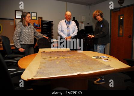 Susan Anderson (rechts) bietet einige Einblicke in die Flagge des Bundesstaates Indiana, die sie als Artefakt an das Hampton Roads Naval Museum spendet, an den Museumserzieher Zach Smyers (Mitte) und die stellvertretende Direktorin Toni Deetz-Rock (links). Die Flagge gehörte Andersons Vater, dem verstorbenen Captain Walter "Jack" Deal, USN, der während des Vietnamkriegs der befehlshabende Offizier des River Assault Squadron 15 war. Damals war es üblich, dass Bootskapitäne während des Vietnamkriegs die Staatsflagge ihres Heimatstaates auf ihren Flussangriffsbooten führten. Stockfoto