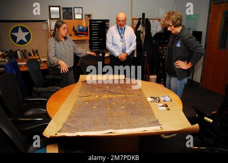 Susan Anderson (rechts) bietet einige Einblicke in die Flagge des Bundesstaates Indiana, die sie als Artefakt an das Hampton Roads Naval Museum spendet, an den Museumserzieher Zach Smyers (Mitte) und die stellvertretende Direktorin Toni Deetz-Rock (links). Die Flagge gehörte Andersons Vater, dem verstorbenen Captain Walter "Jack" Deal, USN, der während des Vietnamkriegs der befehlshabende Offizier des River Assault Squadron 15 war. Damals war es üblich, dass Bootskapitäne während des Vietnamkriegs die Staatsflagge ihres Heimatstaates auf ihren Flussangriffsbooten führten. Stockfoto