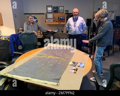 Susan Anderson (rechts) bietet einige Einblicke in die Flagge des Bundesstaates Indiana, die sie als Artefakt an das Hampton Roads Naval Museum spendet, an den Museumserzieher Zach Smyers (Mitte) und die stellvertretende Direktorin Toni Deetz-Rock (links). Die Flagge gehörte Andersons Vater, dem verstorbenen Captain Walter "Jack" Deal, USN, der während des Vietnamkriegs der befehlshabende Offizier des River Assault Squadron 15 war. Damals war es üblich, dass Bootskapitäne während des Vietnamkriegs die Staatsflagge ihres Heimatstaates auf ihren Flussangriffsbooten führten. Stockfoto