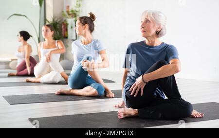 Seniorin, die die geistige und körperliche Gesundheit aufrecht erhält, Yoga-Gruppe im Studio besucht, Stretching Posen praktiziert Stockfoto