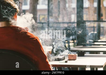 Rückblick auf einen Mann, der im Café Zigaretten raucht. Ungesunder Lebensstil. Stockfoto