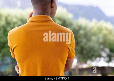 Bild der Rückansicht eines birassischen Mannes in orangefarbenem Kurzarm-Poloshirt mit Kopierraum Stockfoto