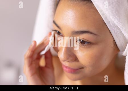 Nahaufnahme einer glücklichen, birassischen Frau, die Handtuch reinigende Gesicht im Badezimmer trägt Stockfoto