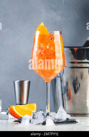 Aperol Spritz klassischer alkoholischer Cocktail in Weinglas, Sommer Italienisch Low Alkohol kalt Drink. Prosecco-Flasche in Eiseimer auf grauem Gegenmesser Stockfoto