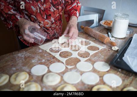 Alte Frau schneidet Puffteig für Knödel. Innenraum Stockfoto