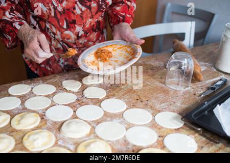 Nicht wiedererkennbare Frau, die Knödel mit Thunfisch, gekochtem Ei und Tomatensoße füllt. Küche Stockfoto