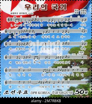 2019 nordkoreanische Briefmarke mit Noten und Texten für das patriotische Lied „Our National Flag“ mit nationalen Symbolen. Stockfoto