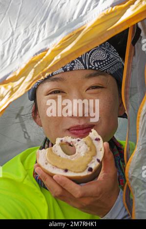 Porträt einer Asiatin in einem Zelt, die einen Bagel mit Erdnussbutter isst Stockfoto