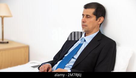 Ein hübscher junger Mann, der die Augen geschlossen hält und zu Hause in einem bequemen Bett sitzt Stockfoto