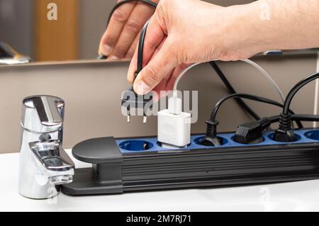 Nahaufnahme einer Frau, die einen Stecker in eine Steckdose im Badezimmer steckt Stockfoto